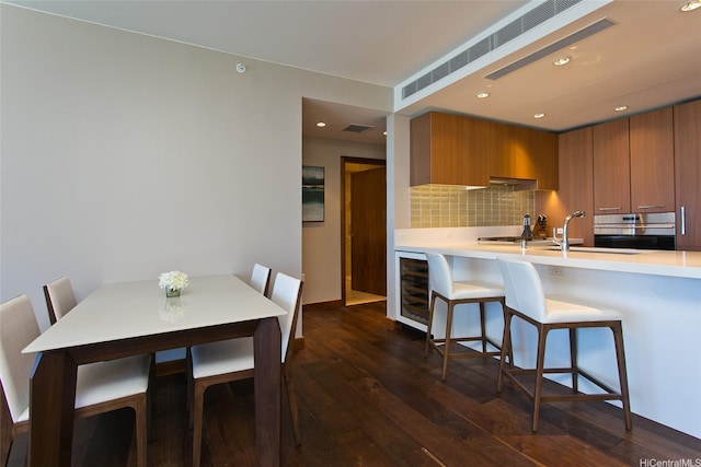 1555 Kapiolani Blvd Unit 1205, Honolulu, HI 96814 - kitchen featuring wine cooler, brown cabinetry, oven, a kitchen breakfast bar, and dark wood-type flooring