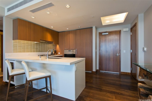 1555 Kapiolani Blvd Unit 1205, Honolulu, HI 96814 - kitchen with brown cabinets, stainless steel oven, a peninsula, a kitchen bar, and dark wood-type flooring