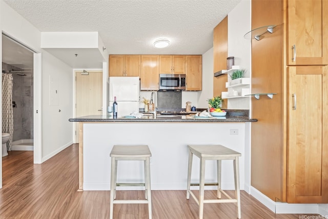 1133 Waimanu St Unit 2503, Honolulu, HI 96814 - kitchen featuring freestanding refrigerator, stainless steel microwave, a peninsula, light wood-style floors, and a breakfast bar