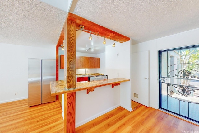 95-312 Kahikinui Ct Unit 213, Mililani, HI 96789 - kitchen featuring stainless steel refrigerator, light wood-style flooring, a breakfast bar, a textured ceiling, and light countertops