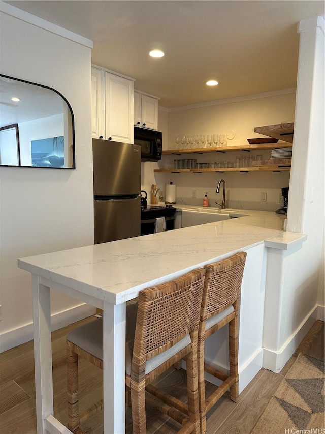 57-68 Eleku Kuilima Pl Unit 657, Kahuku, HI 96731 - kitchen featuring black appliances, a breakfast bar, a peninsula, white cabinetry, and light wood-type flooring
