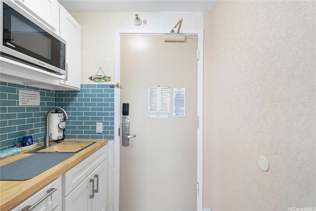 444 Kanekapolei St Unit 501, Honolulu, HI 96815 - kitchen featuring stainless steel microwave, butcher block countertops, tasteful backsplash, and white cabinetry