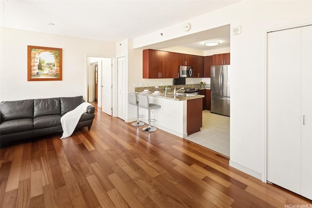 909 Kapiolani Blvd Unit 2002, Honolulu, HI 96814 - kitchen with appliances with stainless steel finishes, open floor plan, a peninsula, light wood-style flooring, and a kitchen breakfast bar