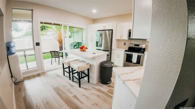 91-950 Laaulu St Unit 42E, Ewa Beach, HI 96706 - kitchen featuring appliances with stainless steel finishes, white cabinetry, light wood finished floors, decorative backsplash, and a kitchen island