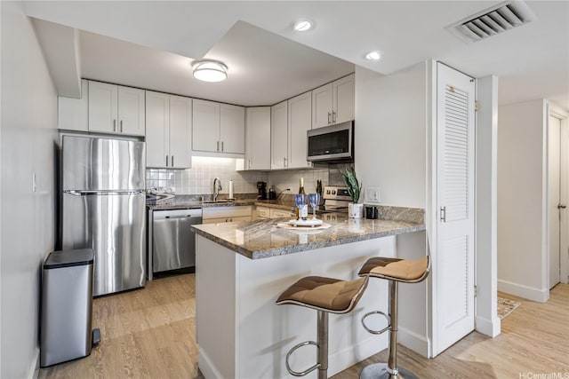 1860 Ala Moana Blvd Unit 1208, Honolulu, HI 96815 - kitchen with appliances with stainless steel finishes, light wood-style floors, a peninsula, tasteful backsplash, and white cabinetry