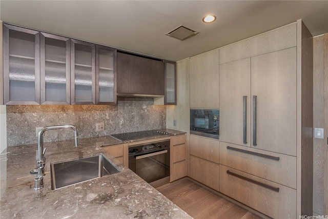 1000 Auahi St Unit 2007, Honolulu, HI 96814 - kitchen with black appliances, dark stone counters, glass insert cabinets, light wood finished floors, and decorative backsplash
