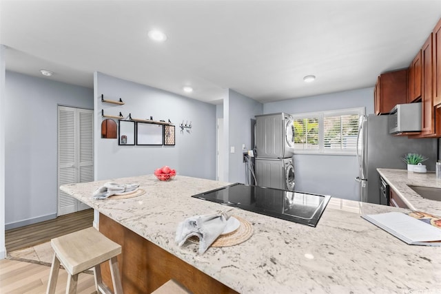 44-130-5 Mui Pl Unit 2605, Kaneohe, HI 96744 - kitchen featuring black electric stovetop, stacked washer / dryer, light stone countertops, light wood-style flooring, and a kitchen bar