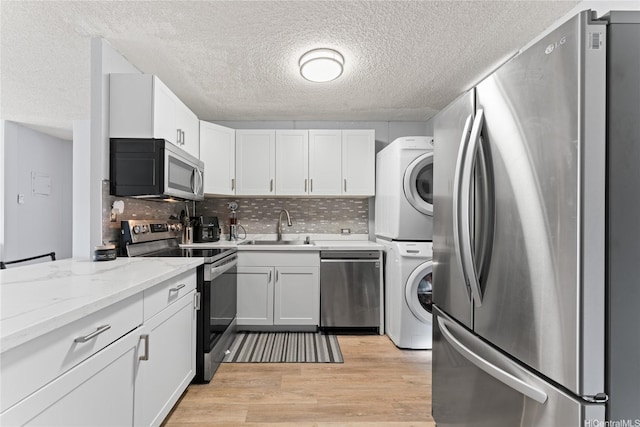 95-2035 Waikalani Pl Unit B303, Mililani, HI 96789 - kitchen with stainless steel appliances, stacked washing machine and dryer, light wood-style flooring, white cabinets, and a textured ceiling