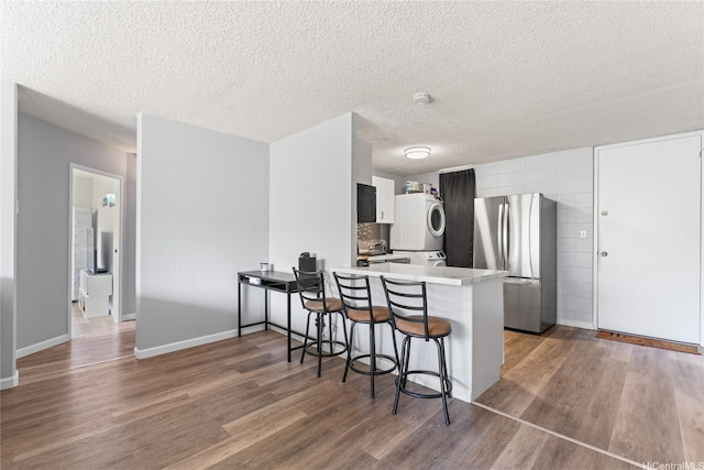 95-2035 Waikalani Pl Unit B303, Mililani, HI 96789 - kitchen featuring freestanding refrigerator, estacked washer and dryer, a peninsula, wood finished floors, and a breakfast bar
