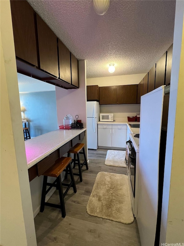 1616 Kewalo St Unit 303, Honolulu, HI 96822 - kitchen with wood finished floors, dark brown cabinets, white appliances, light countertops, and a textured ceiling