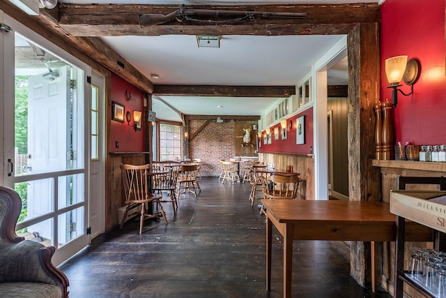 dining room with plenty of natural light, brick wall, dark wood-type flooring, and beamed ceiling