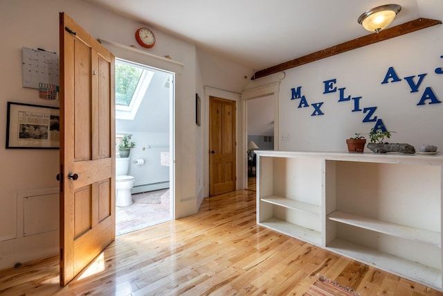 interior space with lofted ceiling with skylight, baseboard heating, and light hardwood / wood-style floors