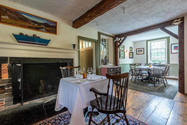 dining area with a textured ceiling, a baseboard radiator, wood-type flooring, and beamed ceiling