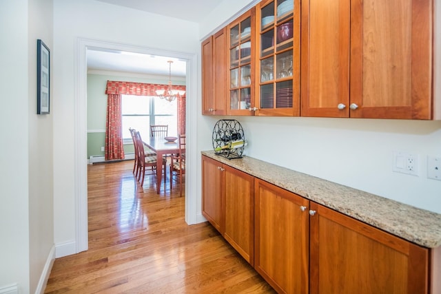 kitchen with light wood-type flooring, light stone counters, a notable chandelier, decorative light fixtures, and ornamental molding