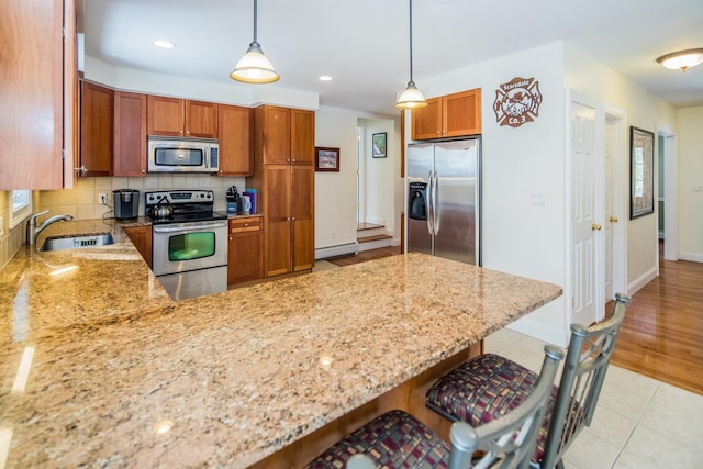 kitchen with hanging light fixtures, backsplash, appliances with stainless steel finishes, a breakfast bar, and sink