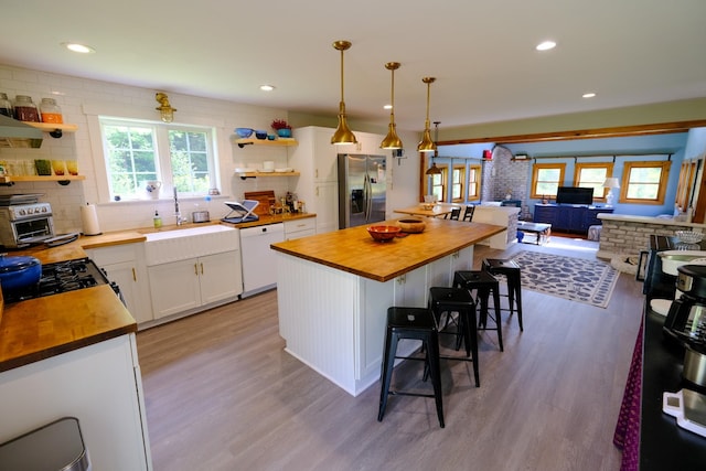 kitchen featuring stainless steel fridge, a sink, white dishwasher, open shelves, and wood counters