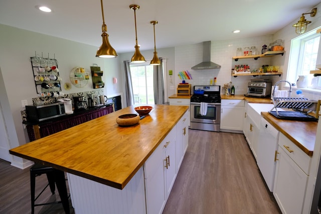 kitchen with butcher block counters, plenty of natural light, wall chimney range hood, and appliances with stainless steel finishes