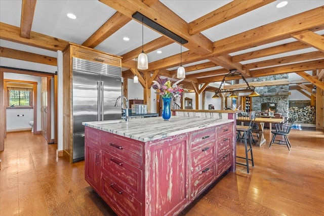 kitchen featuring dark wood-type flooring, an island with sink, light stone countertops, hanging light fixtures, and a kitchen breakfast bar