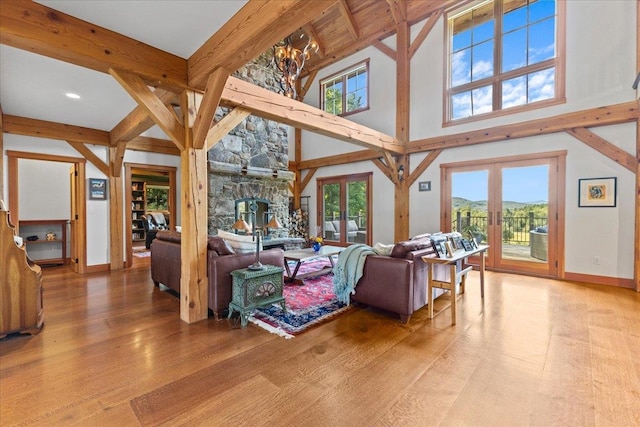 living room featuring french doors, a chandelier, light hardwood / wood-style floors, a fireplace, and beam ceiling