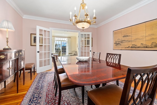 dining space with hardwood / wood-style flooring, ornamental molding, a notable chandelier, and french doors