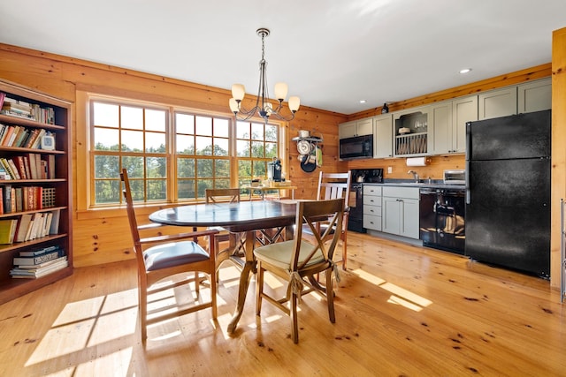 dining room featuring an inviting chandelier, sink, light hardwood / wood-style floors, and wood walls