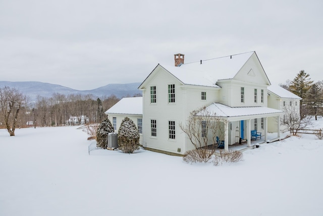 snow covered rear of property with central AC, a porch, and a mountain view