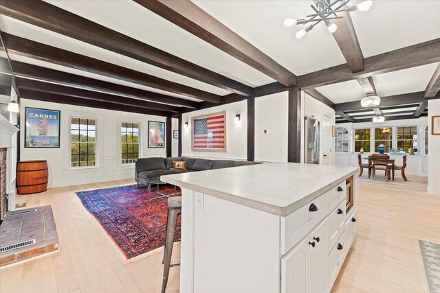 kitchen featuring a breakfast bar area, beamed ceiling, white cabinetry, and light hardwood / wood-style floors