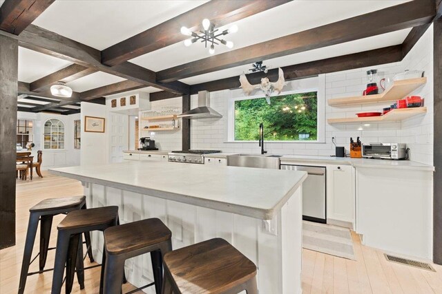 kitchen with wall chimney range hood, an inviting chandelier, tasteful backsplash, and beamed ceiling