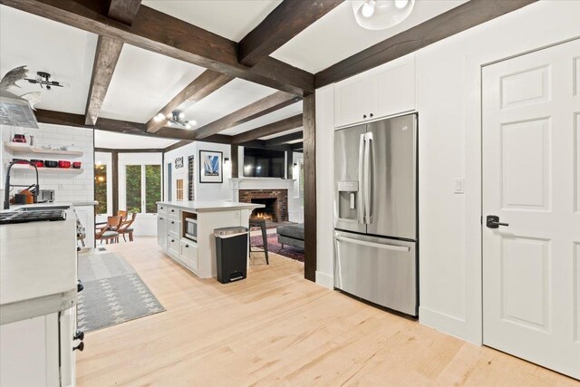 kitchen with beamed ceiling, stainless steel appliances, white cabinetry, and a fireplace