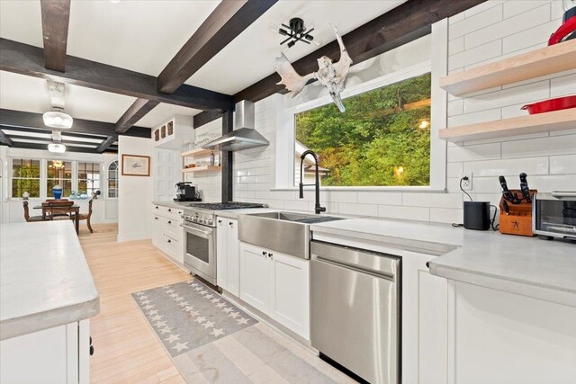 kitchen featuring appliances with stainless steel finishes, light wood-type flooring, white cabinets, wall chimney range hood, and tasteful backsplash