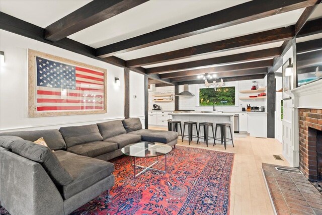 living room with light hardwood / wood-style floors, a brick fireplace, and beam ceiling