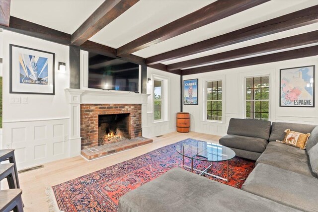 living room featuring beam ceiling, a healthy amount of sunlight, and a brick fireplace