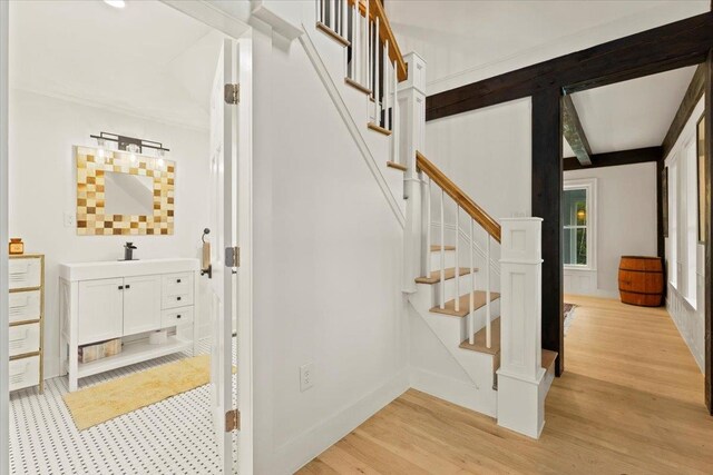 stairway featuring beamed ceiling and light hardwood / wood-style flooring