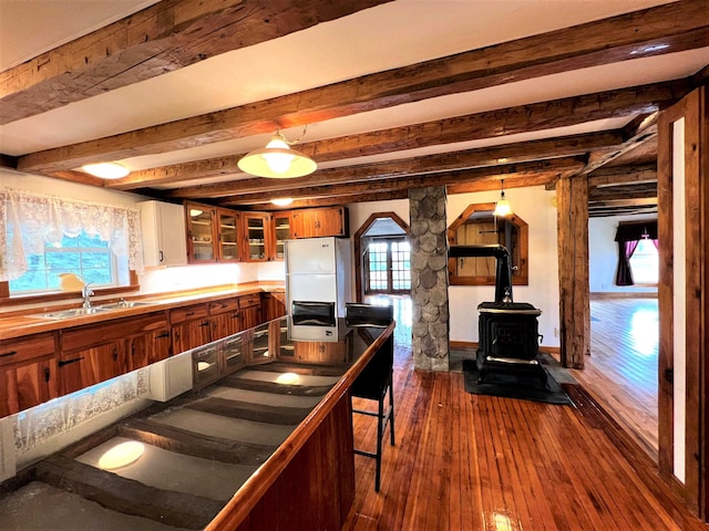 kitchen with white fridge, beamed ceiling, sink, a wood stove, and dark hardwood / wood-style flooring