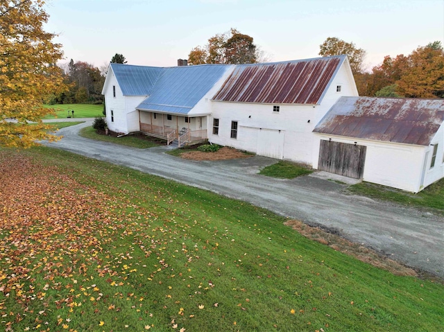 property exterior at dusk with a lawn, an outdoor structure, and a porch