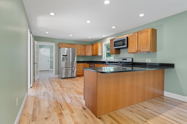 kitchen featuring kitchen peninsula, a barn door, appliances with stainless steel finishes, sink, and light hardwood / wood-style flooring