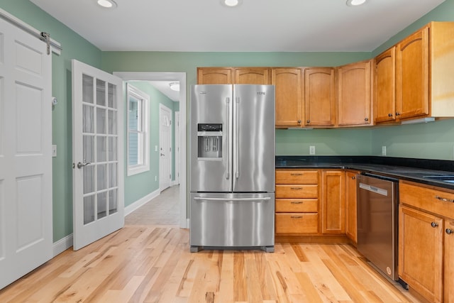 kitchen with a barn door, appliances with stainless steel finishes, sink, and light hardwood / wood-style flooring