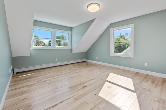 additional living space featuring vaulted ceiling, light hardwood / wood-style floors, a baseboard radiator, and a healthy amount of sunlight