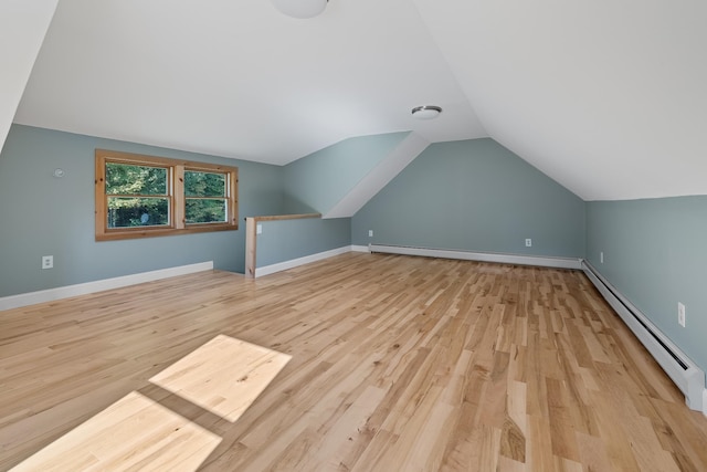 additional living space with a baseboard radiator, vaulted ceiling, and light wood-type flooring