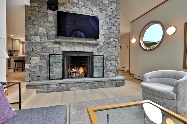 living room with a baseboard heating unit, lofted ceiling, light hardwood / wood-style floors, and a stone fireplace