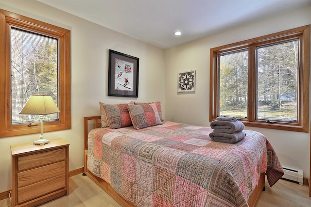 bedroom with multiple windows, a baseboard heating unit, and light hardwood / wood-style flooring