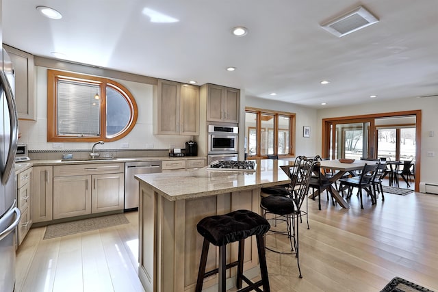 kitchen featuring light stone counters, a kitchen island, a breakfast bar area, stainless steel appliances, and light wood-type flooring