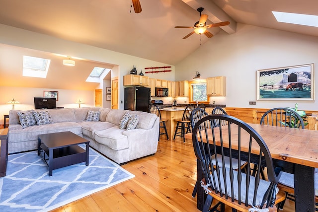 living room with beamed ceiling, high vaulted ceiling, a skylight, light hardwood / wood-style flooring, and ceiling fan