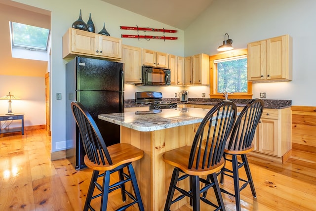 kitchen featuring light brown cabinetry, light wood-type flooring, a breakfast bar, high vaulted ceiling, and black appliances