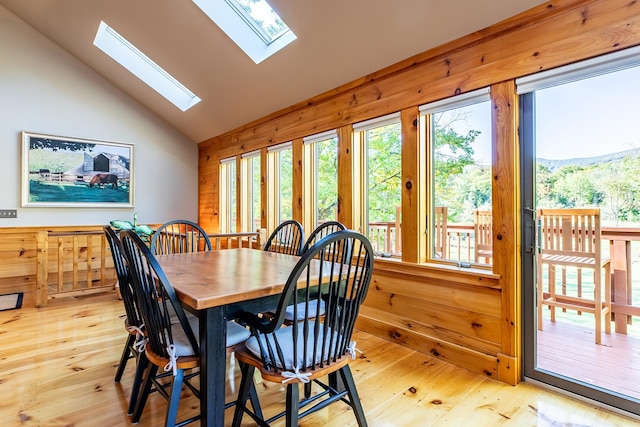 dining room with light hardwood / wood-style floors, vaulted ceiling with skylight, and wooden walls