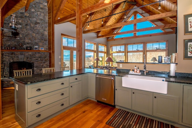 kitchen featuring sink, stainless steel dishwasher, kitchen peninsula, dark stone counters, and a fireplace