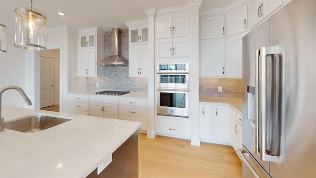 kitchen featuring sink, hanging light fixtures, appliances with stainless steel finishes, wall chimney range hood, and white cabinets