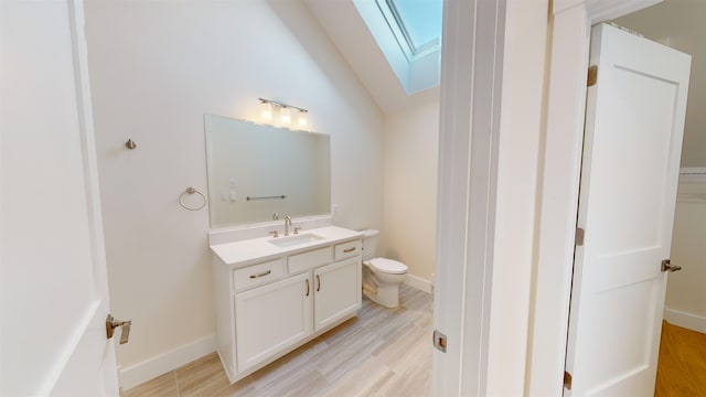 bathroom with toilet, vanity, vaulted ceiling with skylight, and wood-type flooring