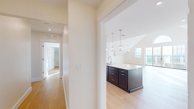 kitchen with pendant lighting, sink, vaulted ceiling, and light hardwood / wood-style floors