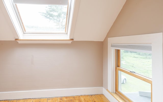 additional living space with a healthy amount of sunlight, vaulted ceiling with skylight, and light hardwood / wood-style flooring